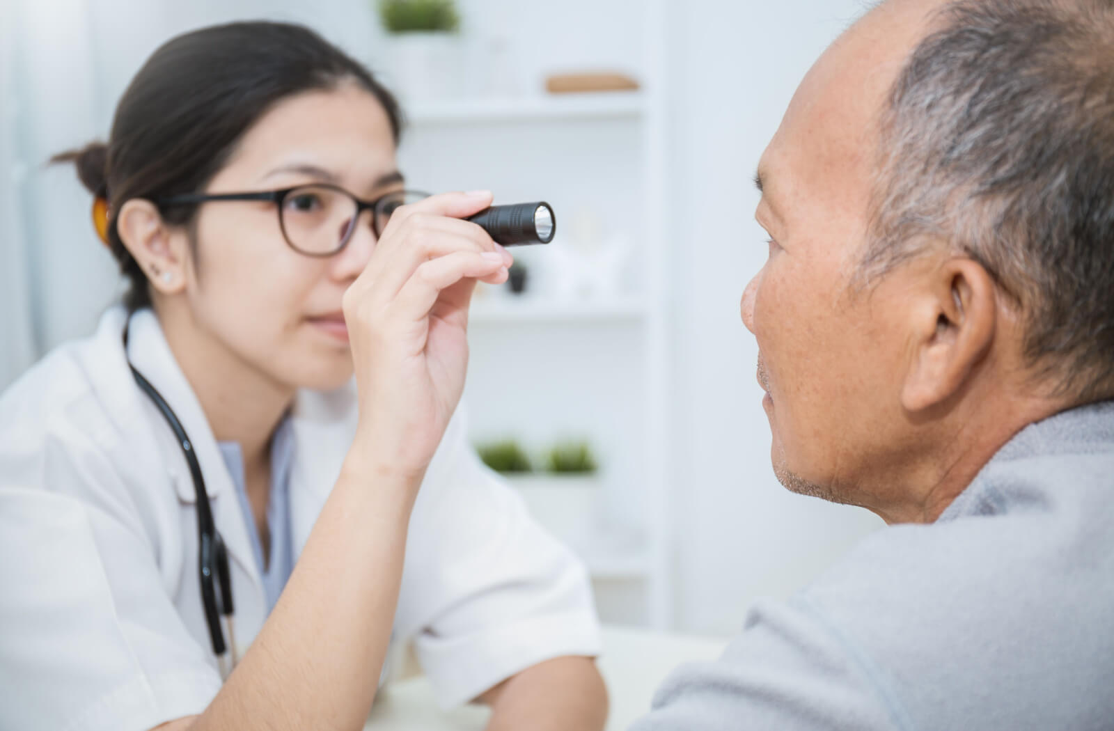 An optometrist examines her patient's eyes with a light.