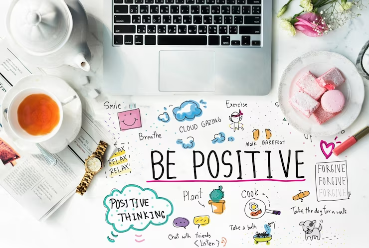 Desk with a laptop, tea, baked goods, and a ‘Be Positive’ poster.