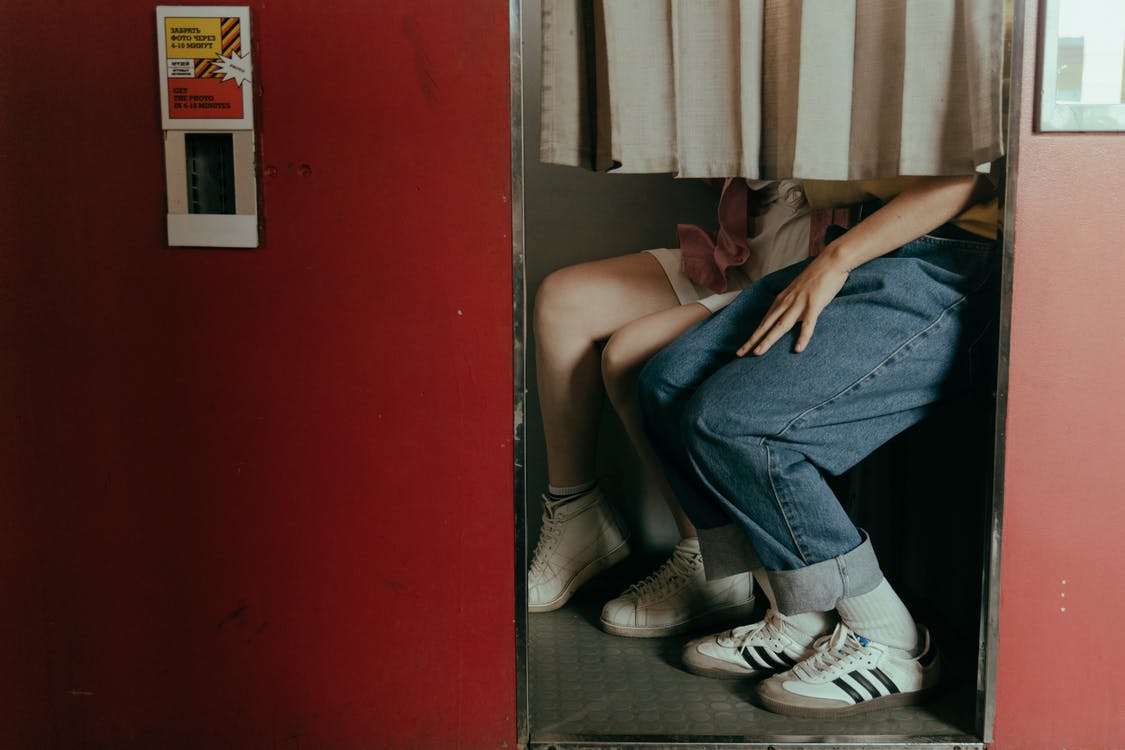 Woman in Blue Denim Jeans and White and Black Adidas Sneakers Sitting on Black Floor