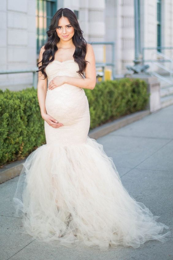 A lady wearing mermaid wedding dress and holding her baby bump