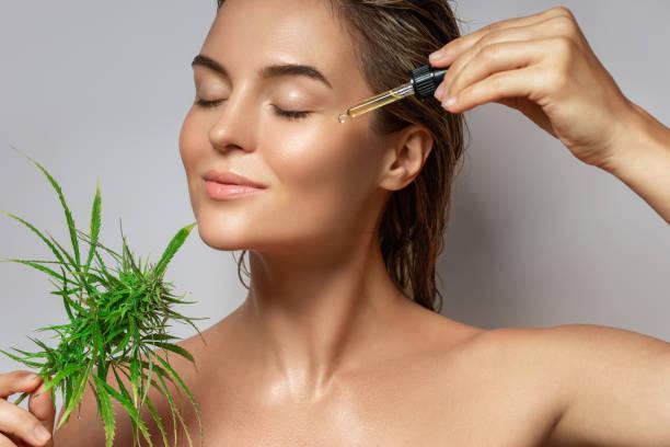 CBD cosmetics concept. Beautiful woman with a cannabis leaf CBD cosmetics concept. Beautiful woman with a cannabis leaf on gray background CBD oil oin skin stock pictures, royalty-free photos & images