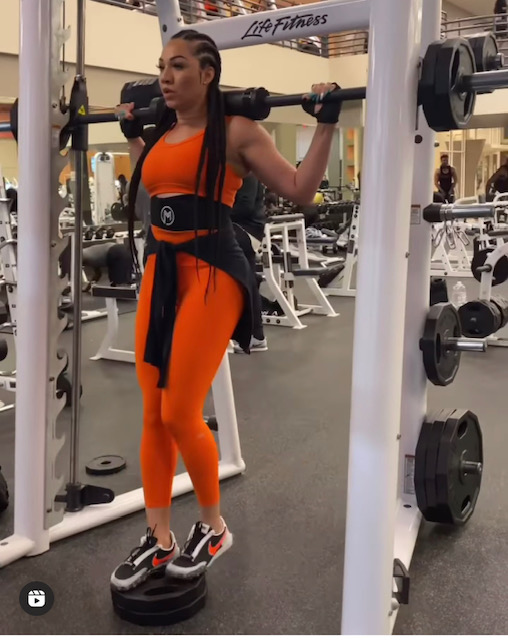 dr eva b in an orange workout outift doing squata
