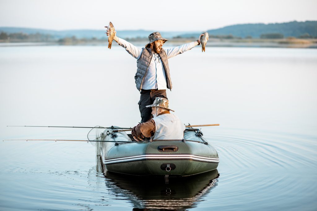 Man standing on a boat in a lake happy and holding fish