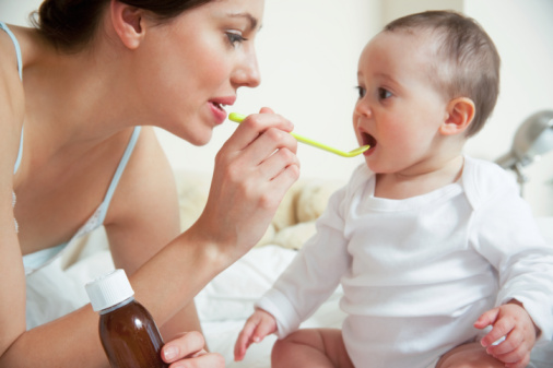Mum administering syrup to baby in bedroom