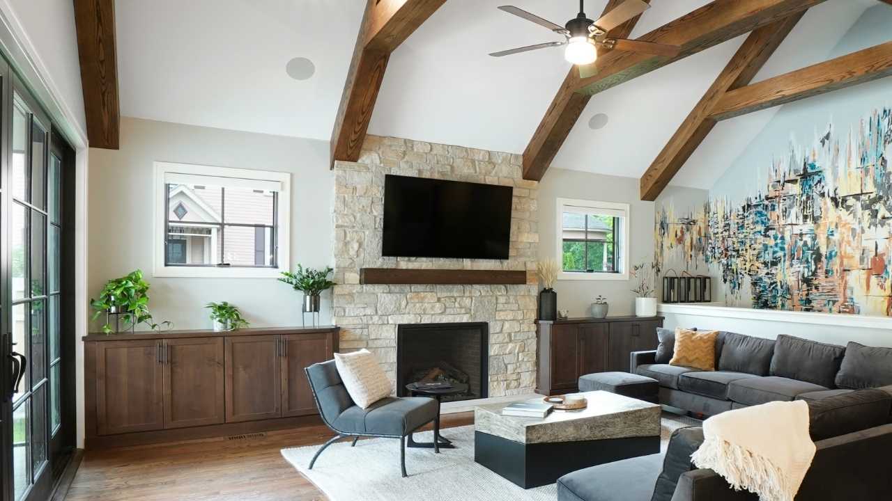 Living Room with flagstone fireplace and built in cabinets on either side. Featuring a gray, modern sectional and chair with a stone and metal coffee table. A contemporary wall mural and trestle ceiling beams add architectural and artistic interest to the space.