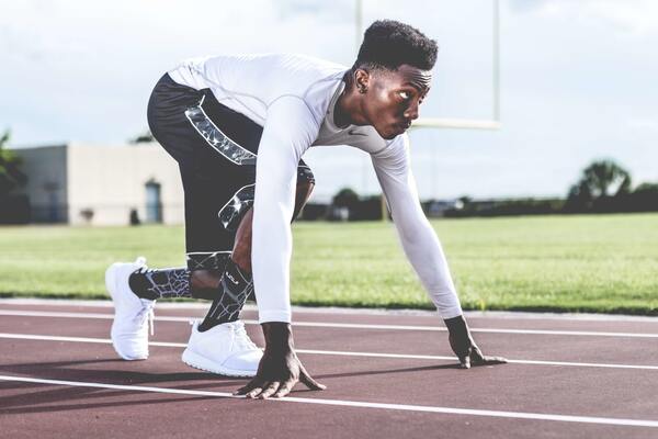 Foto de um homem negro se preparando para correr em uma pista de corrida profisisonal 