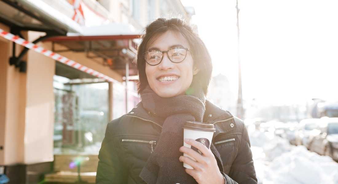 woman walking down street smiling holding coffee