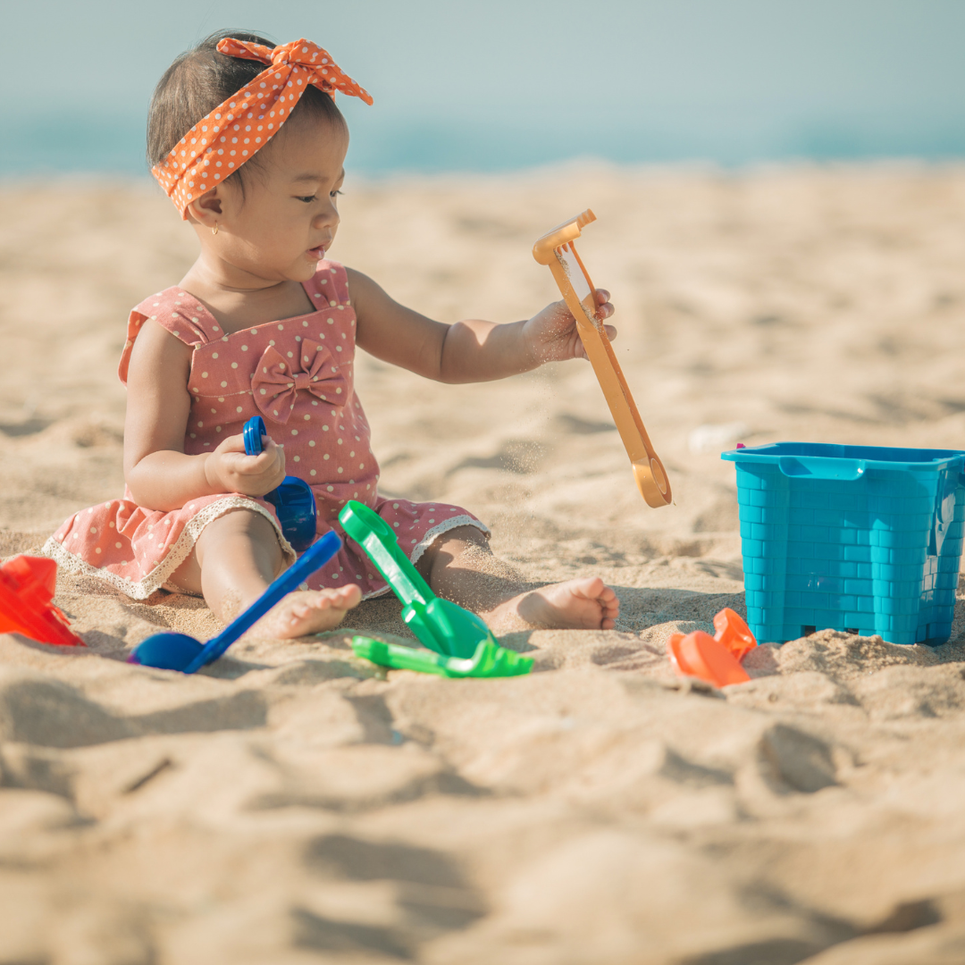 Baby girl playing with toy shovel on the beach outside