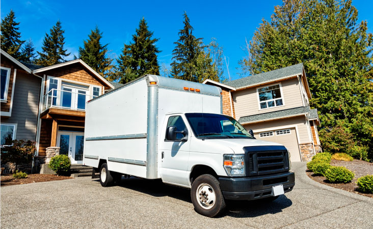 A plain white moving truck backed up to a residential house for loading.