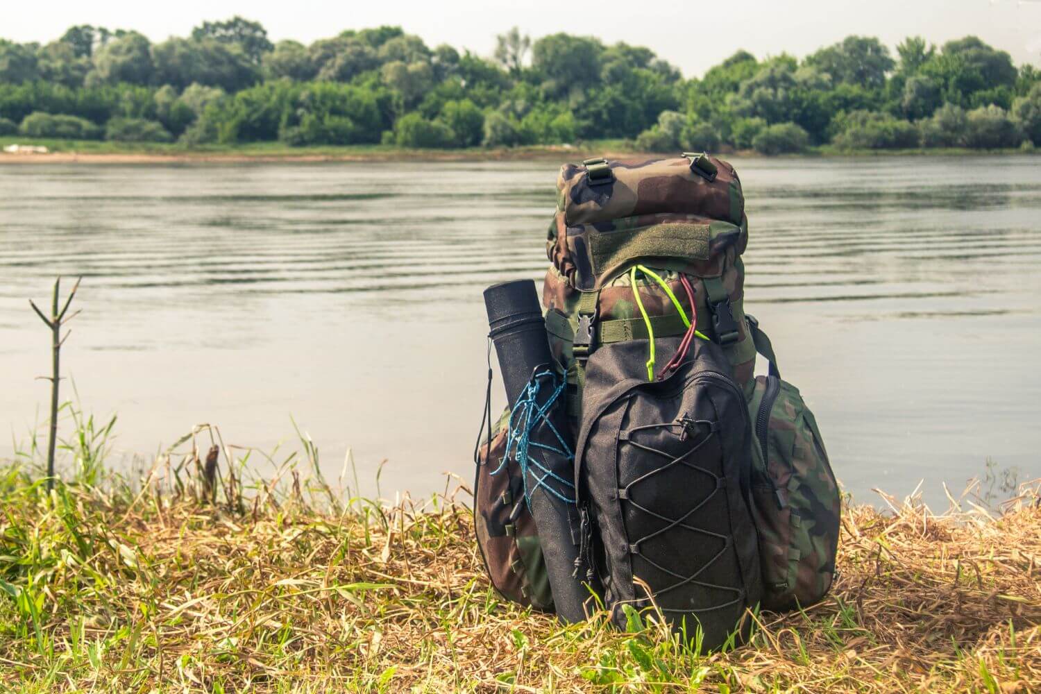 Tactical pack loaded with survival gear sitting on the grass near a lake