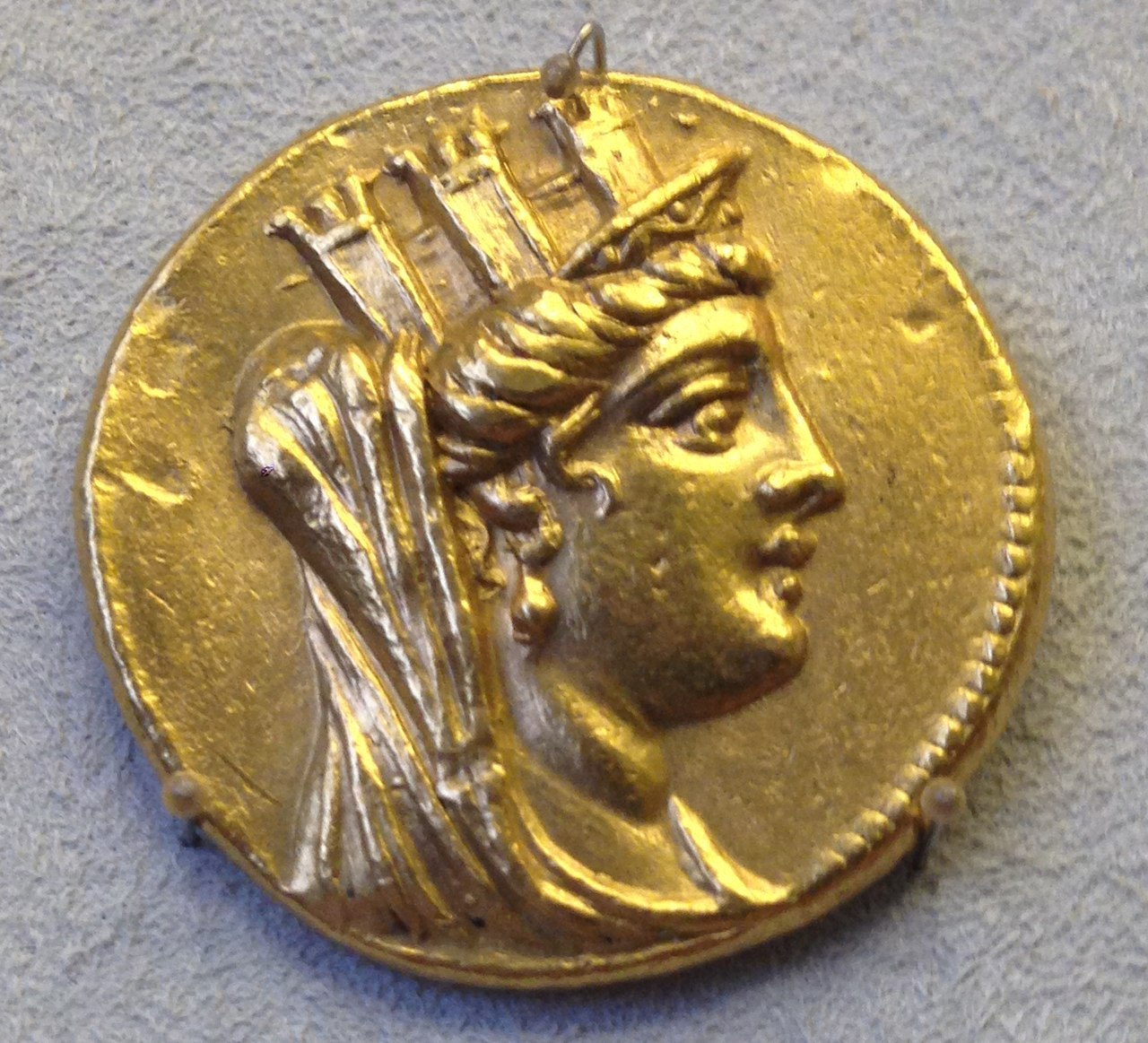 This particular item is a piece of currency fashioned from gold, and upon its surface is a depiction of the image of Tyche.