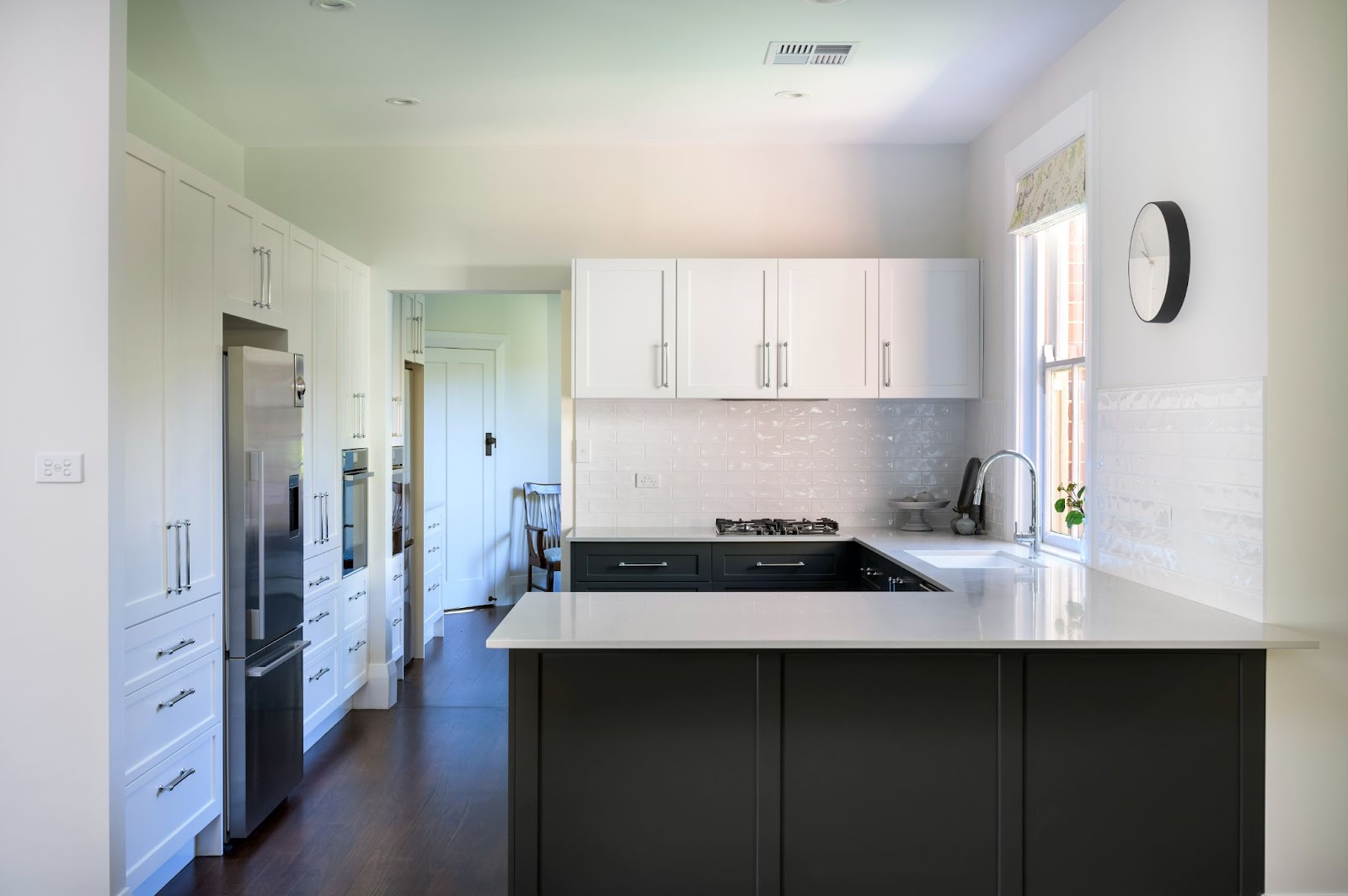 Modern, fully renovated kitchen with white cabinetry, stainless steel appliances, and a black-and-white color scheme, featuring a large island and a bright, airy atmosphere.