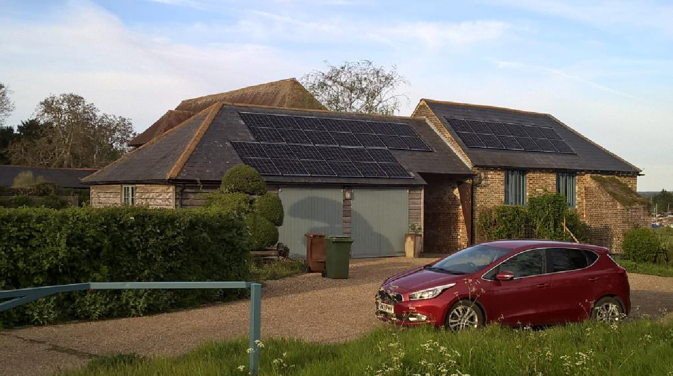 Images shows a grade II listed barn with 3 rows solar PV panels on the roof, which blend into the colour of the roof tiles.