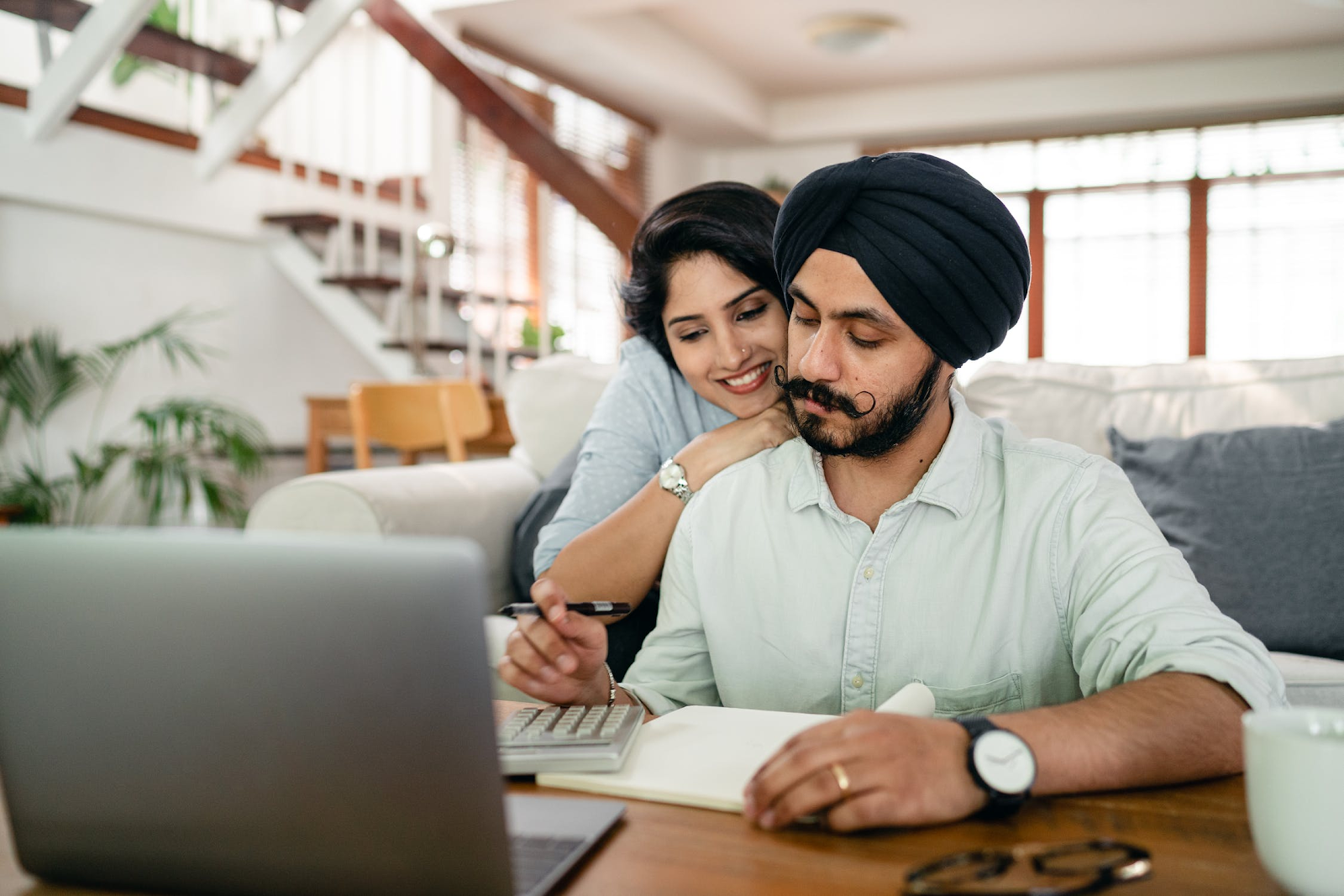 Serious Sikh man using a calculator with wife over his shoulder