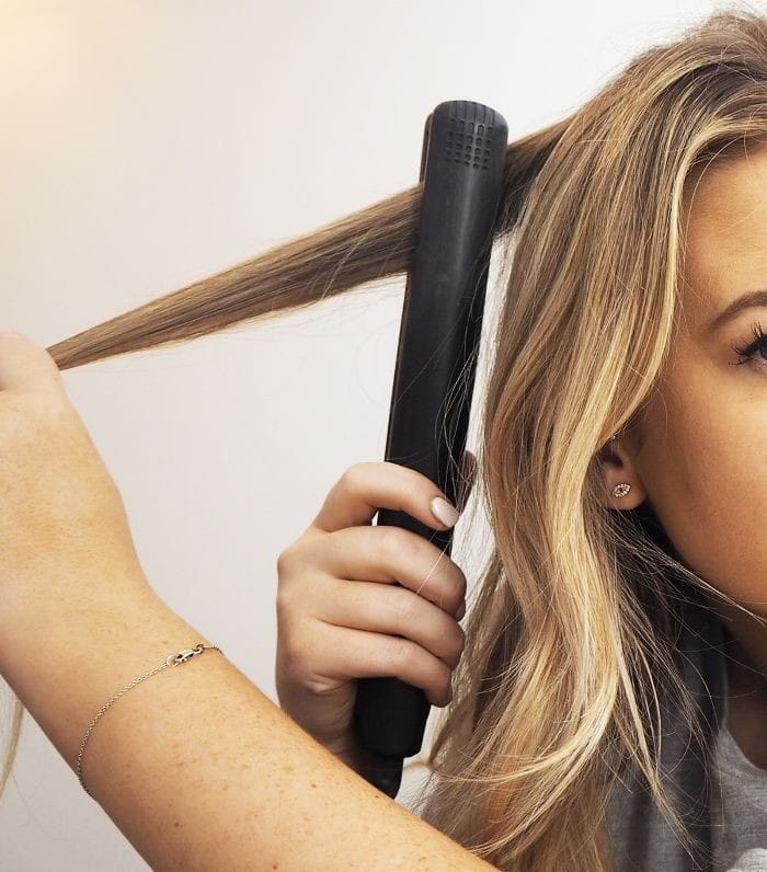 a picture showing a lady trying to make her hair wavy with a hair straightener