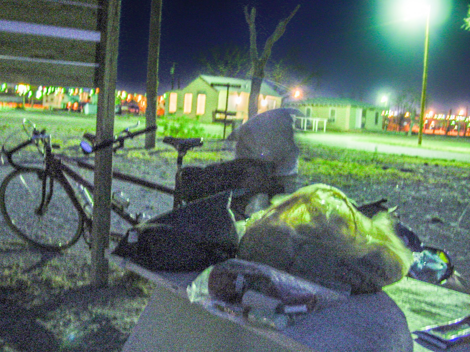 A grainy night photo of a bicycle built for two and camping gear on a picnic table. 