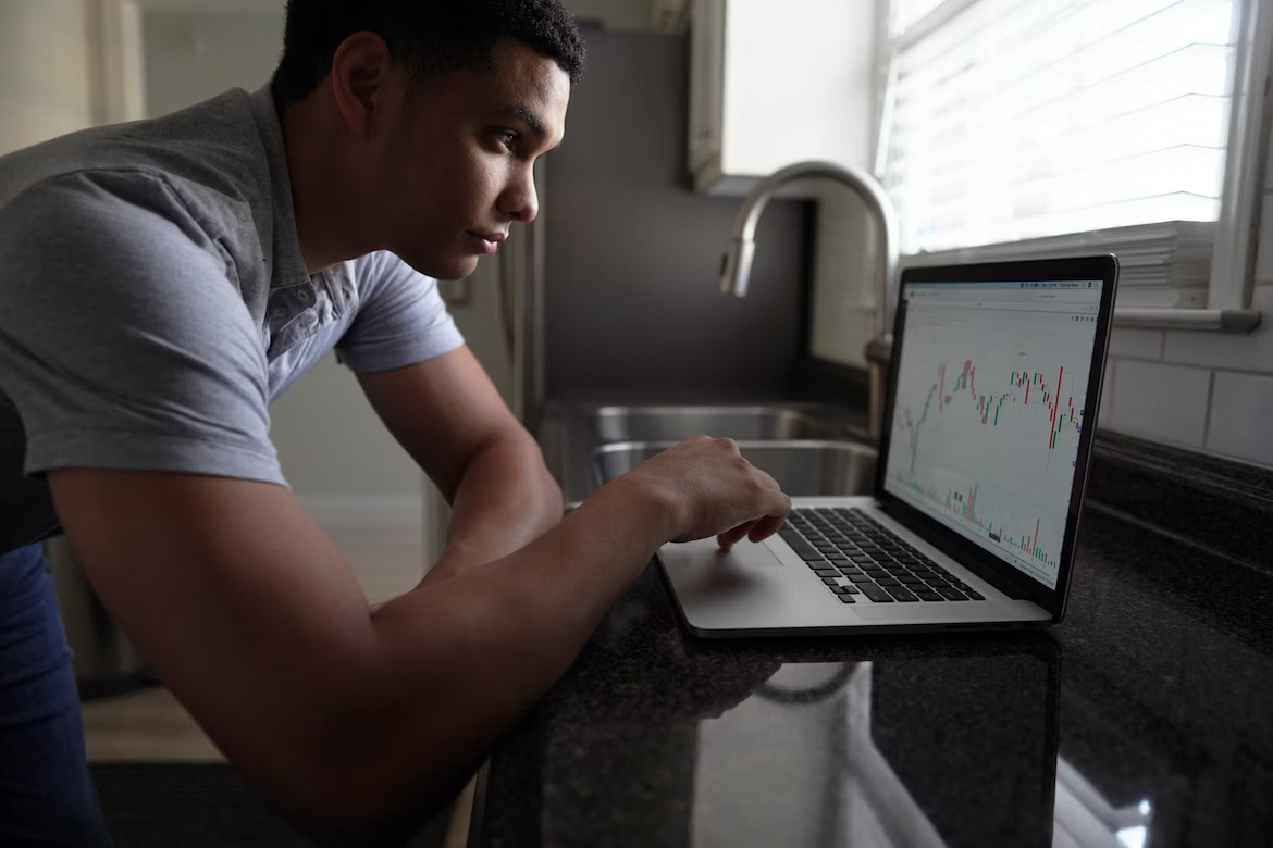 how to use life insurance as a bank - side view of a man looking at the laptop. the screen shows investing graphs 
