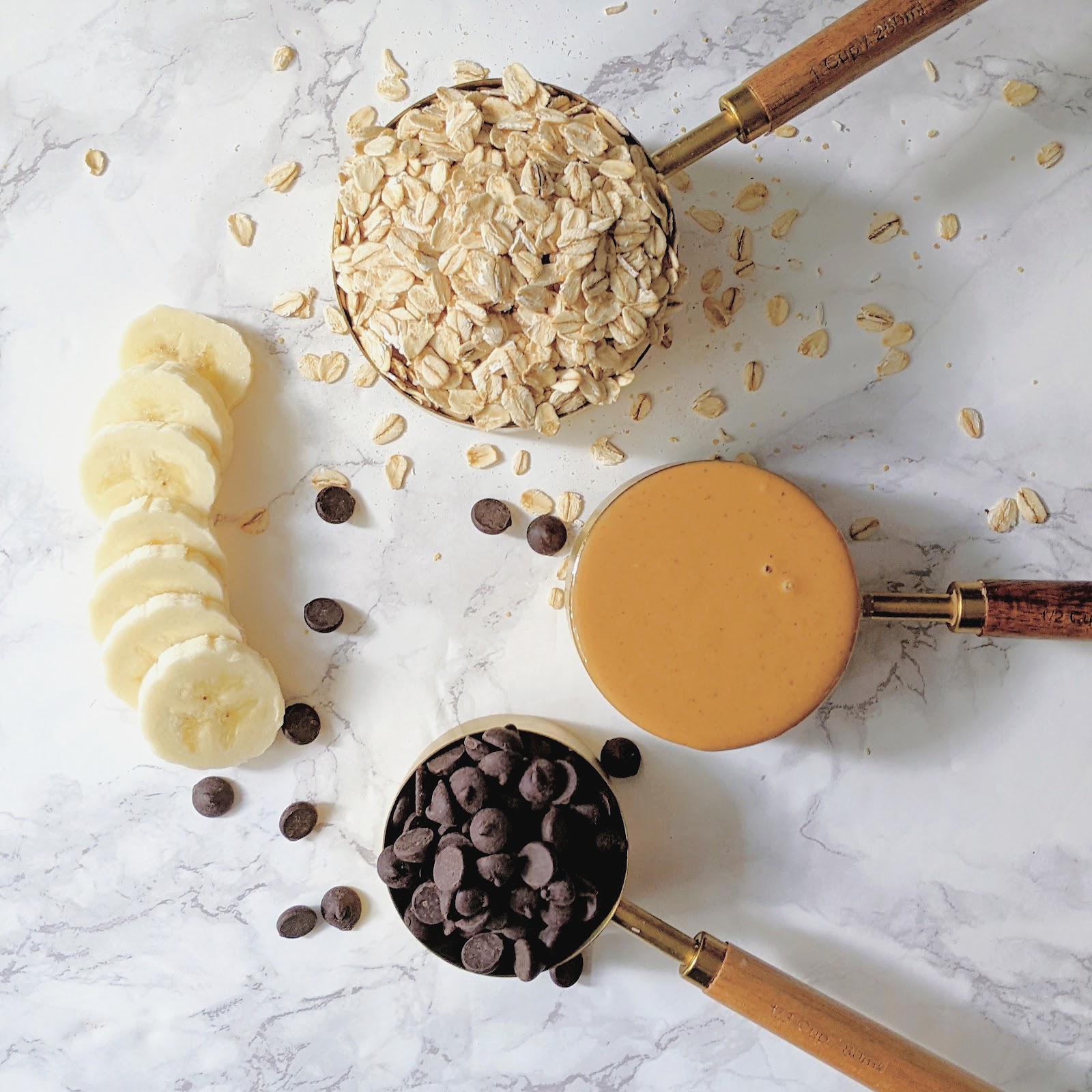 top down view of ingredients needed to make peanut butter cups including peanut butter, banana, chocolate chips, maple syrup and oats