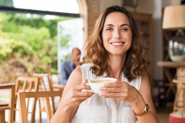 Mature woman at cafeteria Beautiful smiling woman drinking coffee at cafe. Portrait of mature woman in a cafeteria drinking hot cappuccino and looking at camera. Pretty woman with cup of coffee. elderly woman drinking cappuccino stock pictures, royalty-free photos & images