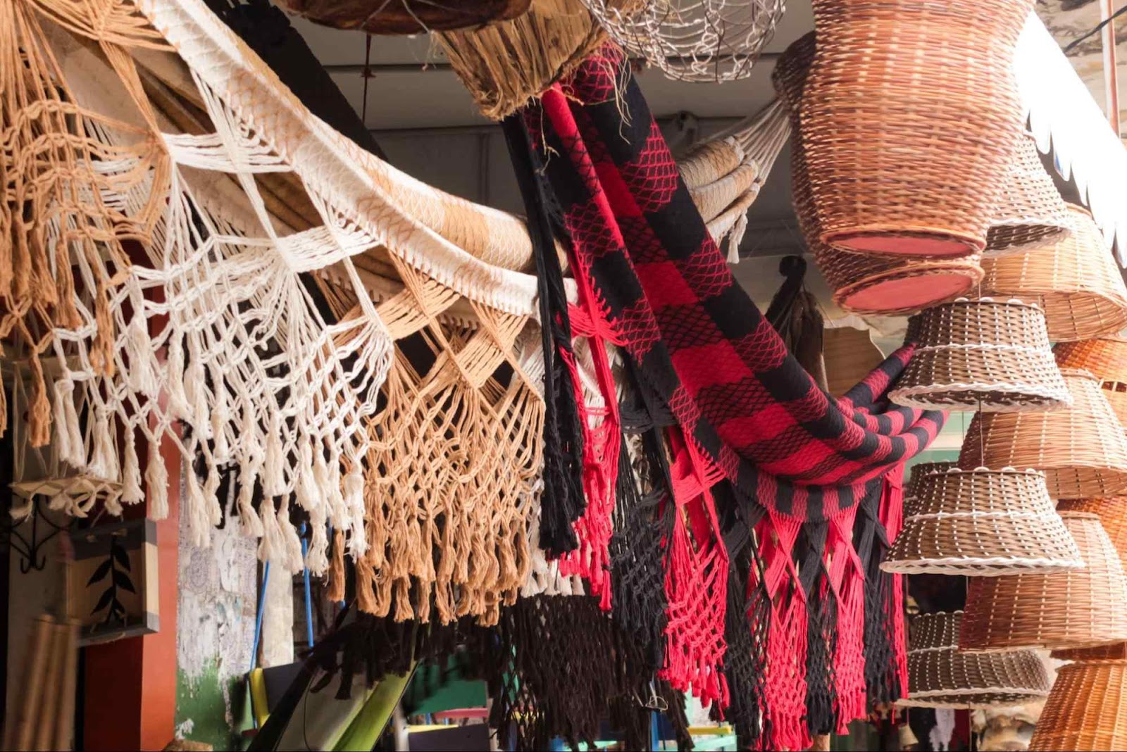 Redes de tecido e cestos de palha artesanais expostos para venda em uma barraquinha de feira.