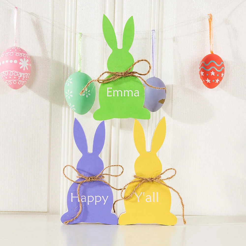 3 lapins de Pâques en bois personnalisés d’un prénom et décorés d’une ficelle nouée autour du cou.