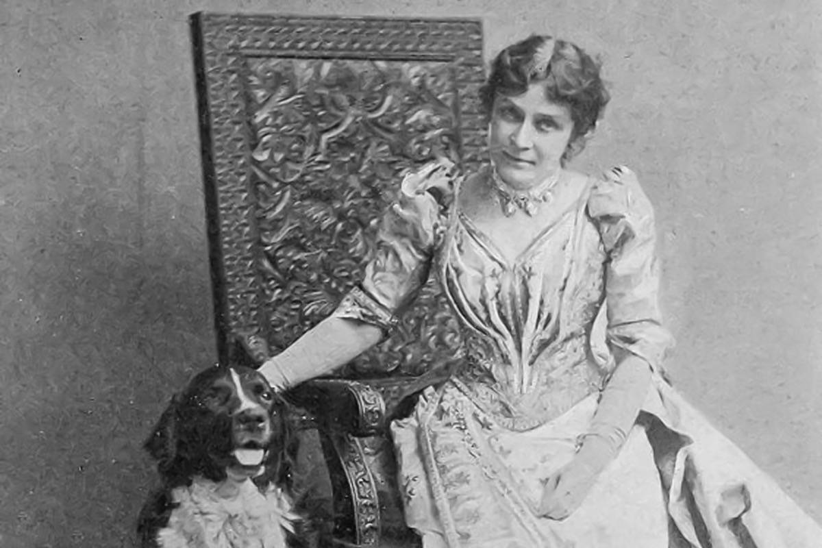 A very old Daguerreotype of a woman sat on a chair - a dog sat beside her. The woman looks to camera with a serious expression.
