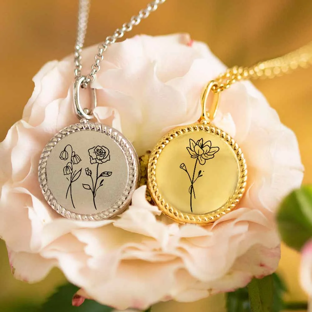 2 colliers médaillon photo, l’un en or, l’autre en argent, avec fleur de naissance gravée sur le couvercle.