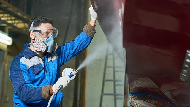Worker wearing mask and googles while spray painting vehicle