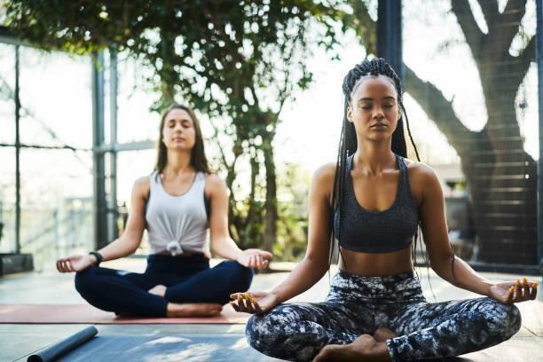 Young woman practicing lotus position with friend Young woman practicing lotus position with friend on porch. Multi-ethnic females are meditating in yoga class. They are in sports clothing. meditating and yoga stock pictures, royalty-free photos & images