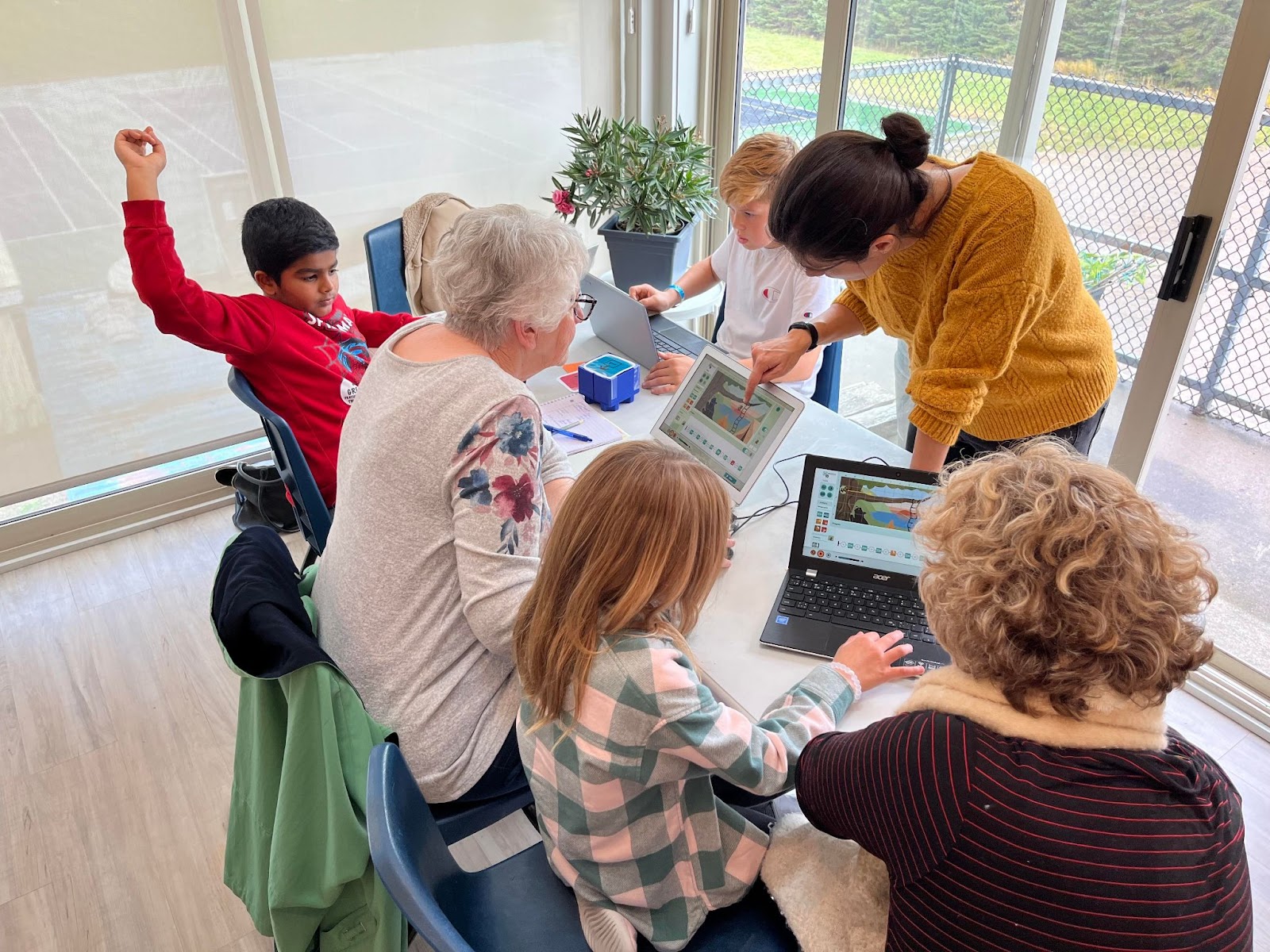 several adults and kids are working on their laptops to create a program in Weavly. 