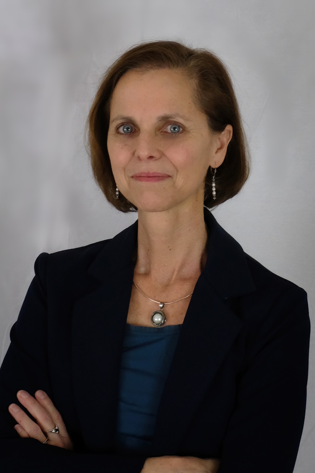 Dr. Daniela Brancaforte is pictured with arms crossed wearing a black blazer with a blue dress underneath.
