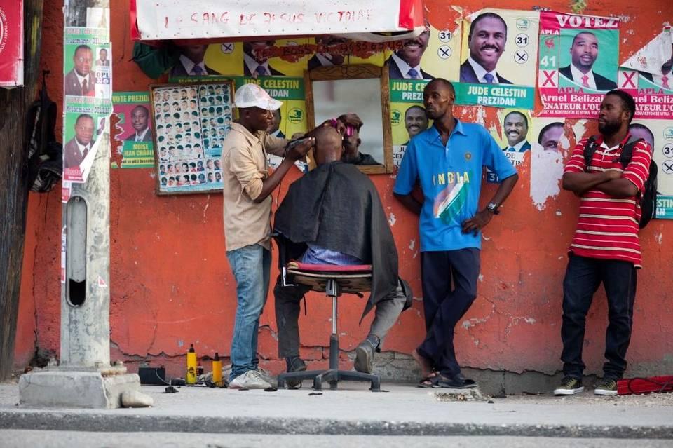 A street barber shop is seen next to a wall decorated with candidates’ posters in Port-au-Prince, Haiti.