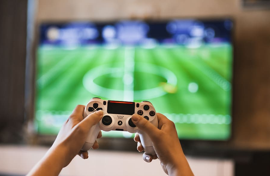 hands holding a game joystick, with a display of a football game in the background