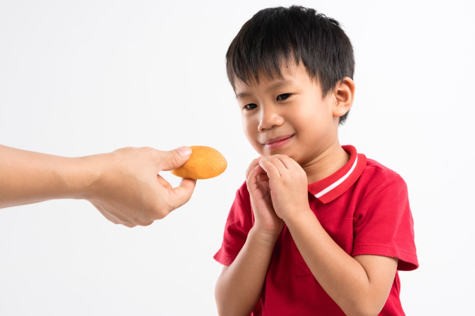 A female hand is giving a snack to Asian kid with the red shirt.