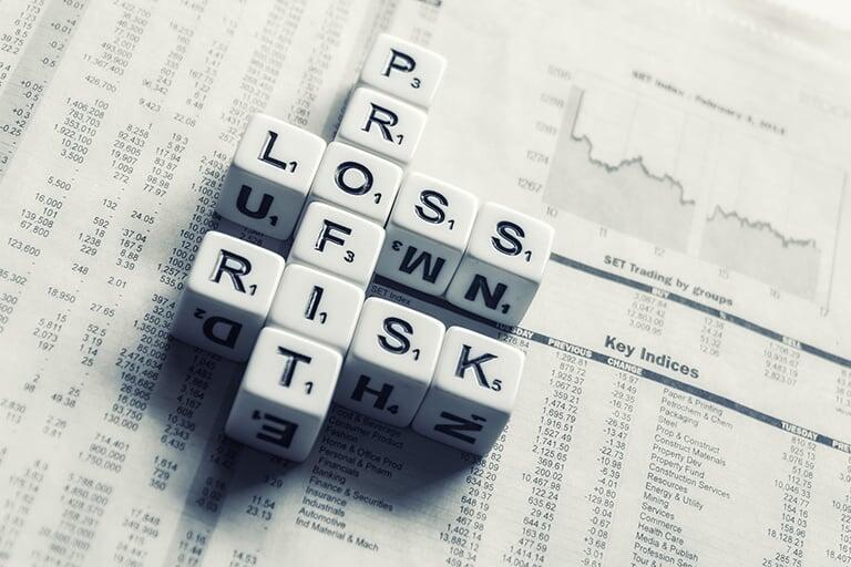 A newspaper with stock prices shown and dice on the newspaper with letters that spell out Profit, Loss and Risk.