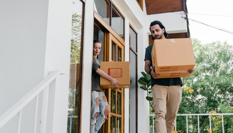 A couple carrying moving boxes out to their portable container.