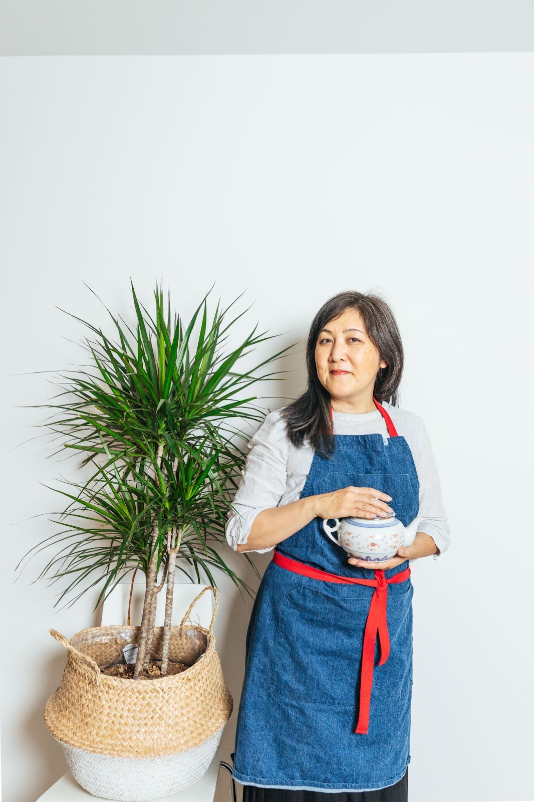 Reclaiming Chinese postpartum traditions founder of Feeding Mama, Mona Stillwell, standing beside a plant and holding a tea cup.