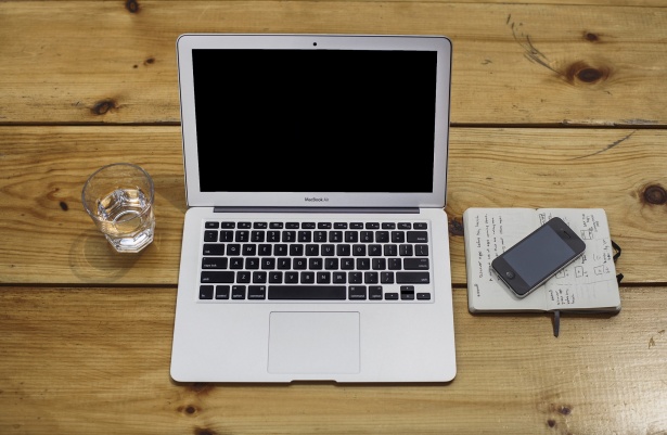 This image shows that Apple MacBook in the table with a glass of water and notes paper with Iphone.