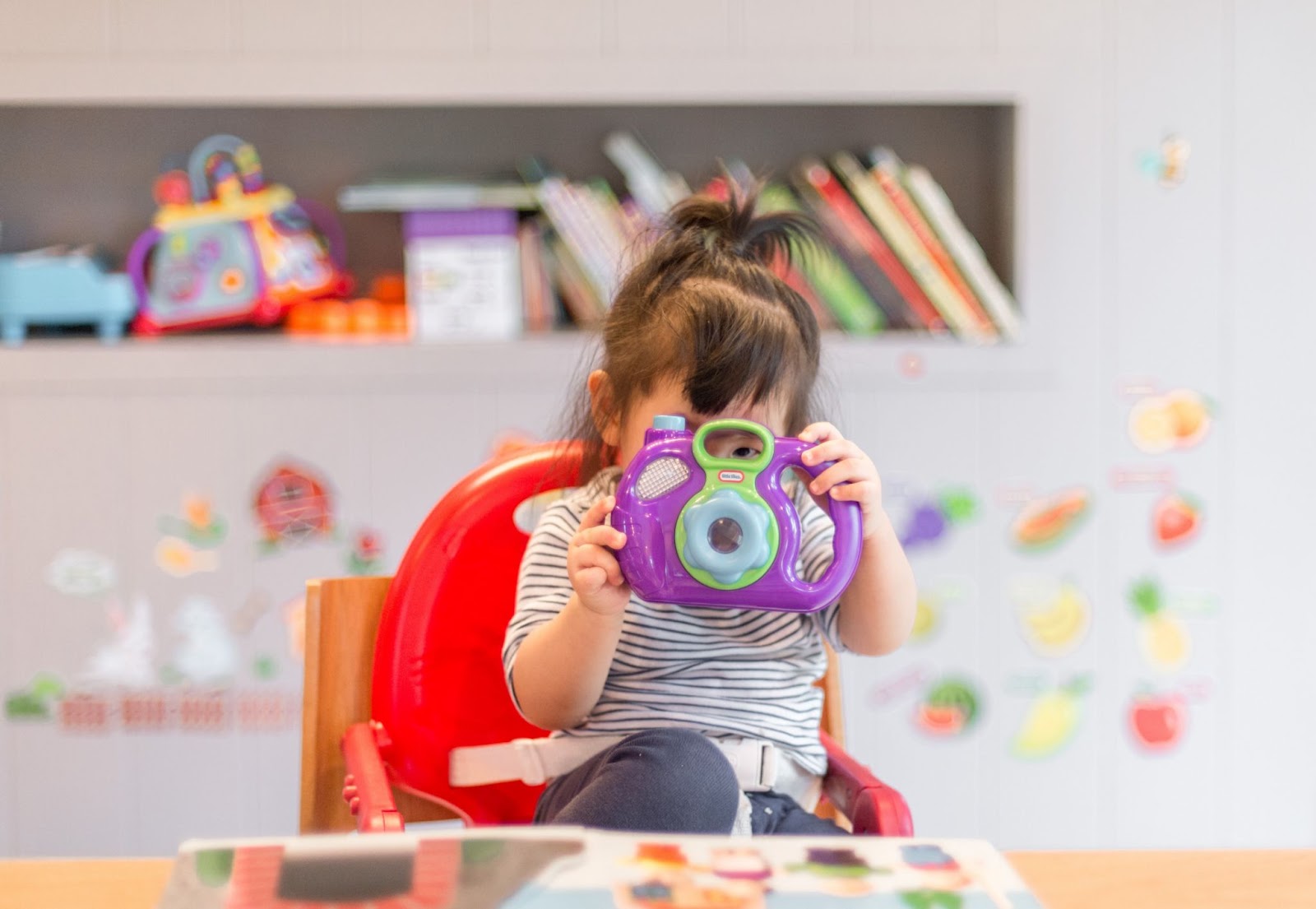 Preschool-aged girl looks through a purple children’s camera lens