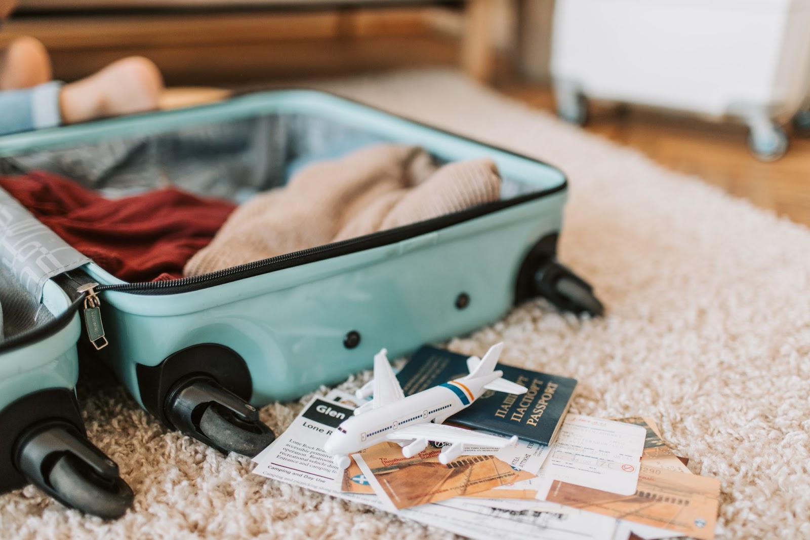 Open suitcase on a carpet with a small toy aeroplane and passport next to it