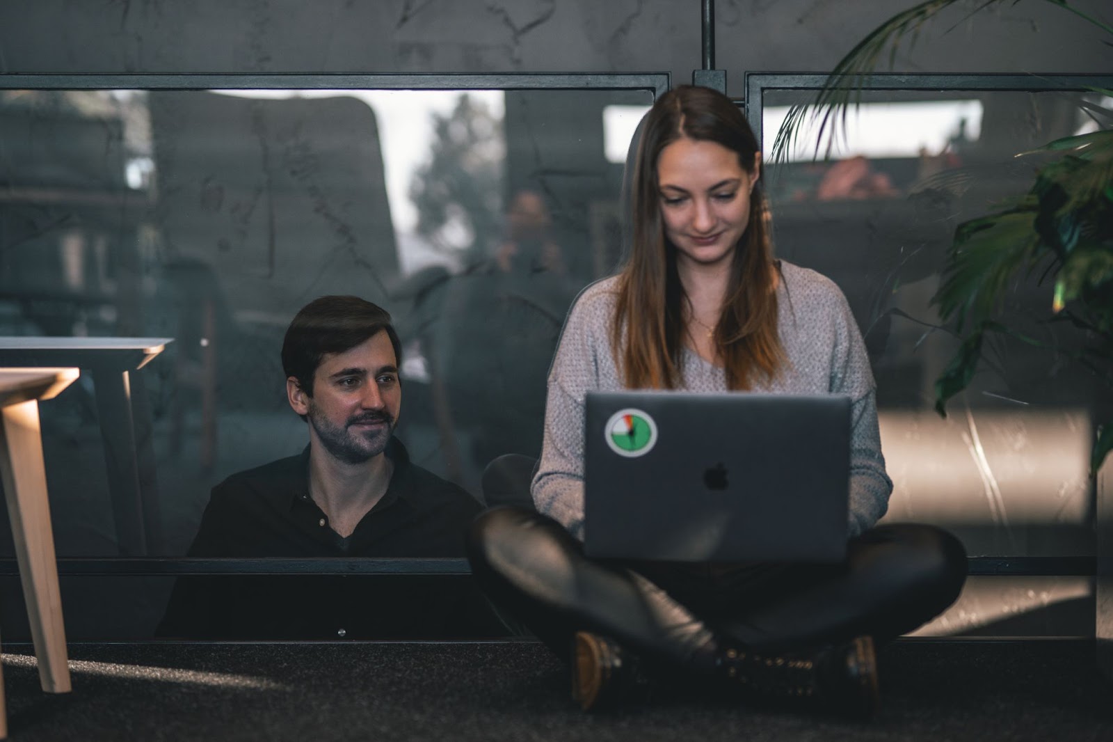 Man behind glass watching woman work on laptop