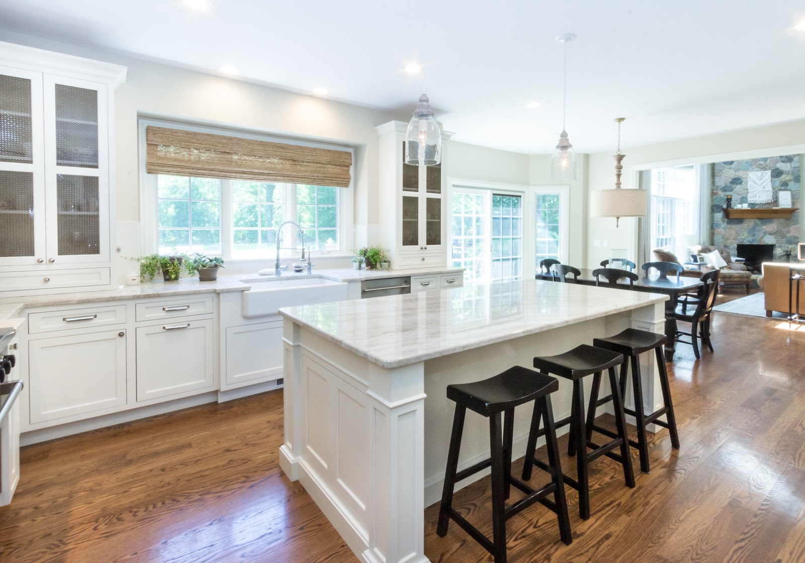 Naturally lit renovated kitchen with white shaker cabinets and glass door display cabinetry, apron sink and eat-in island with quartz countertops.