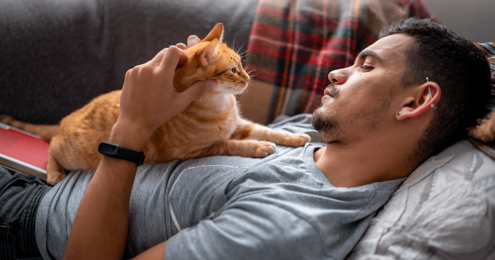 Man laying on couch with orange cat laying on his chest