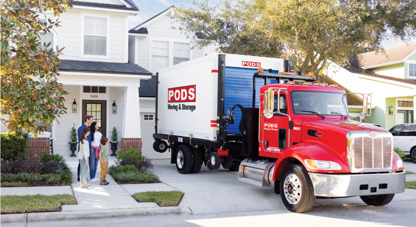A family of four watches as a PODS driver positions their PODS portable moving container in their driveway as they prepare for moving to Canada from the U.S.
