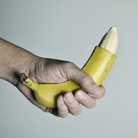 Hand firmly grasping banana with peel cutting off at the top leaving the naked banana at the head