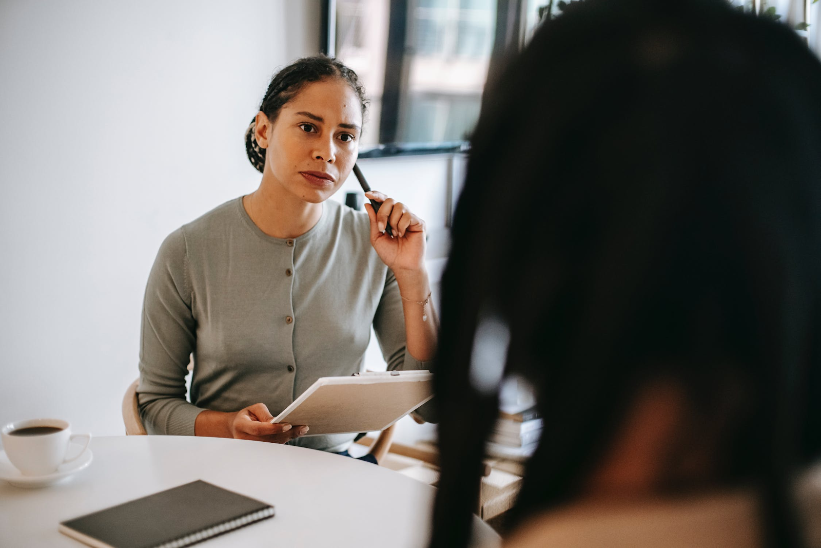 Woman with notebook looking contemplatively at woman in the foreground