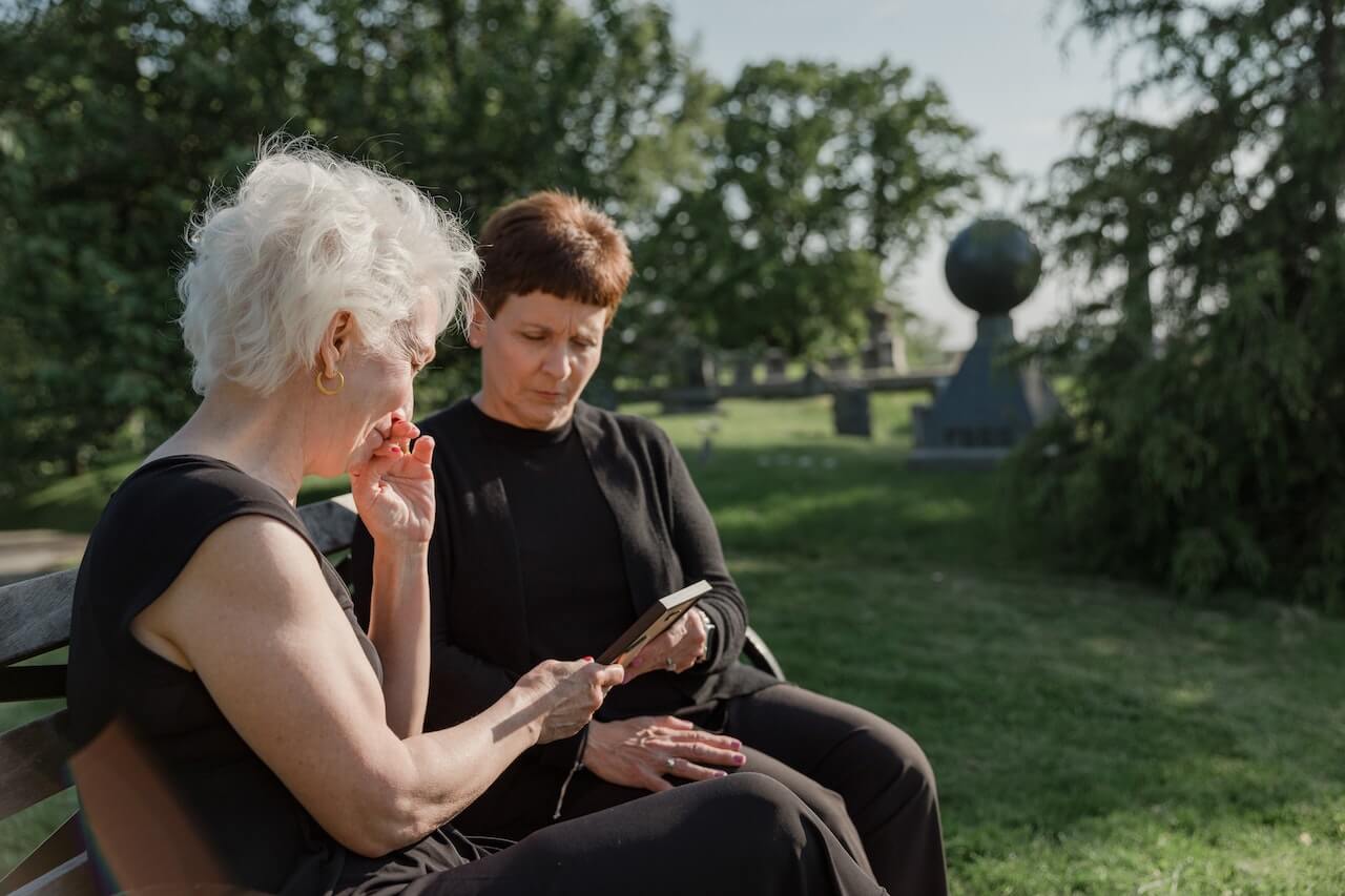 Two women looking at a phone on a bench outside