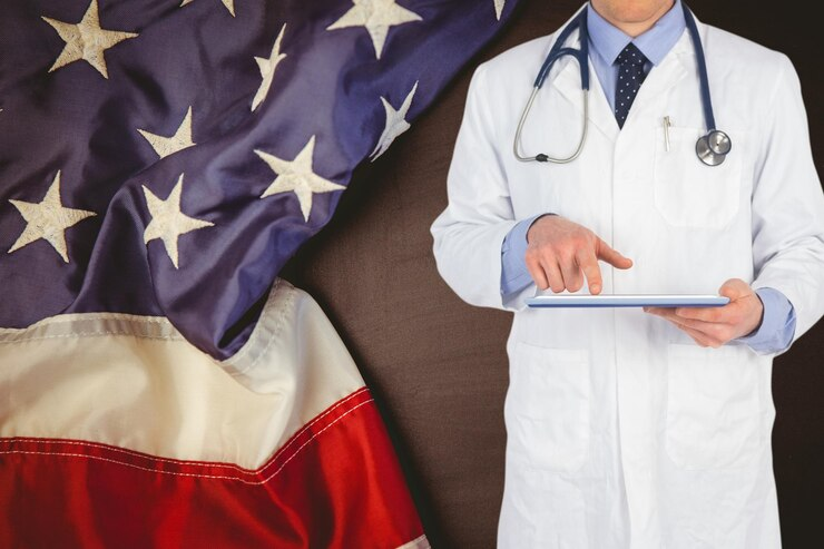 A confident doctor standing against an American flag, symbolising the pursuit of MD/MBBS in the US for UK Medical Students.
