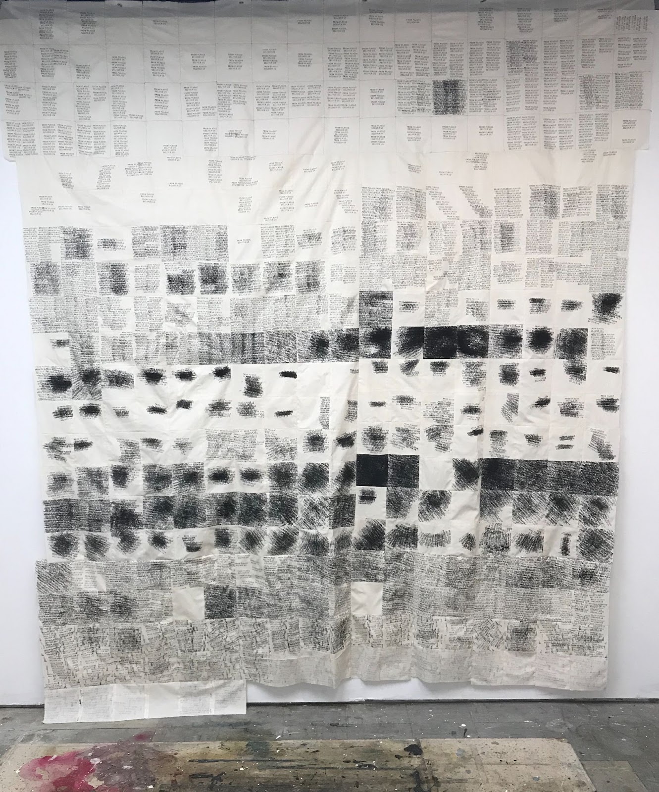 A fifty square foot textile documenting a year of new COVID-19 cases in Johnson county, Iowa. The textile is a cream color and higher case counts are indicated by clusters of overset text in black. It is pieced from 365 squares of 5 by 5 inch fabric.