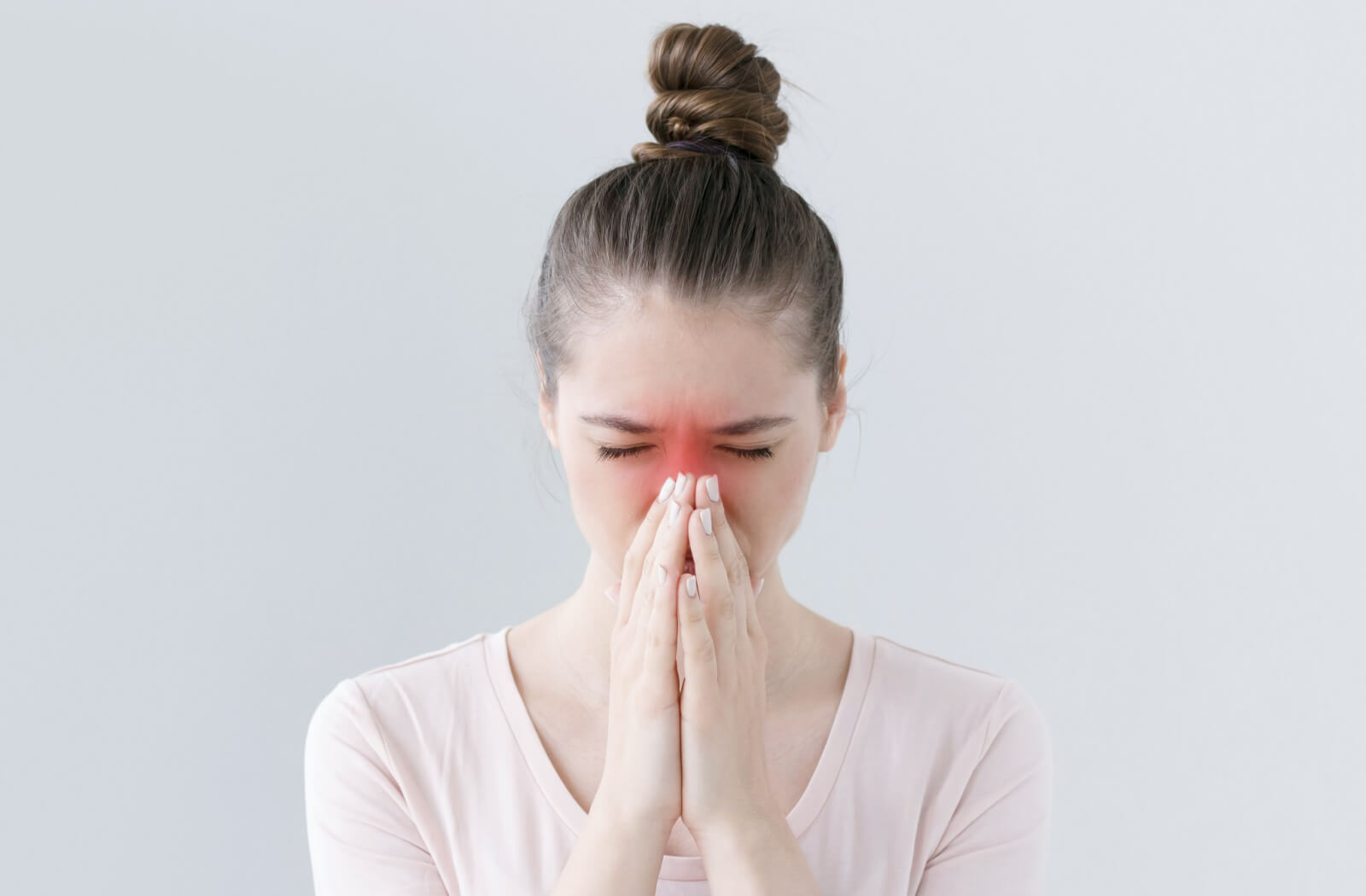 A young female with allergies is covering her nose with her hands with a gesture of pain in her face.